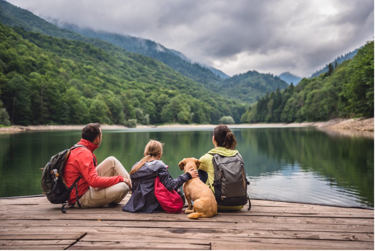 A group of people with their dog sitting on a dock looking at a lake